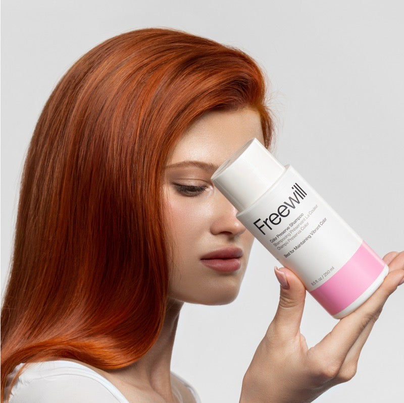 Woman with red hair holding a bottle labeled 'Freewill' against a light background.