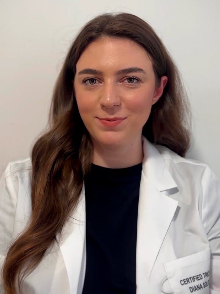 A person wearing a white lab coat against a plain background.